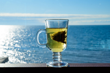 Transparent glass mug with a bag of green leaf tea on a background of the sea.