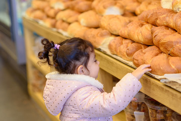 Cute toddler girl in bakery store. Child choosing fresh challah bread loaf in bakery department.