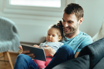 Obraz premium Happy father and his small daughter using touchpad while relaxing at home.