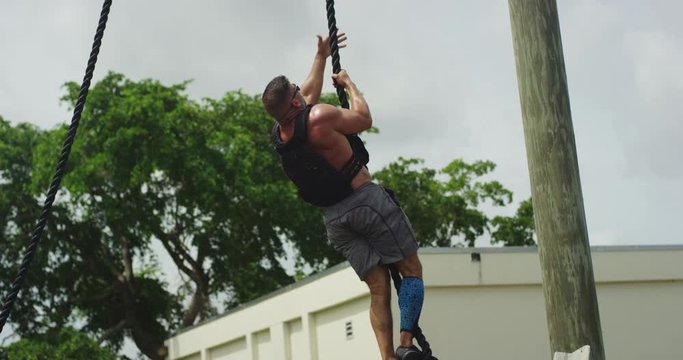 Athletic man climbing rope outside