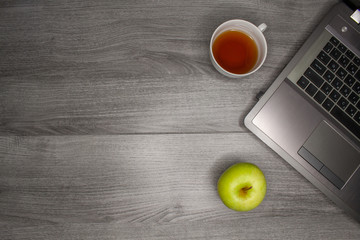 Flat lay of home office. Notebook, green apple and cup of tea on a gray wooden table