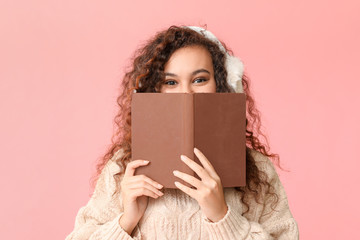 Young woman in warm sweater and with book on color background
