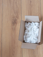 A cardboard box with packing foam pellets top view, on wooden floor