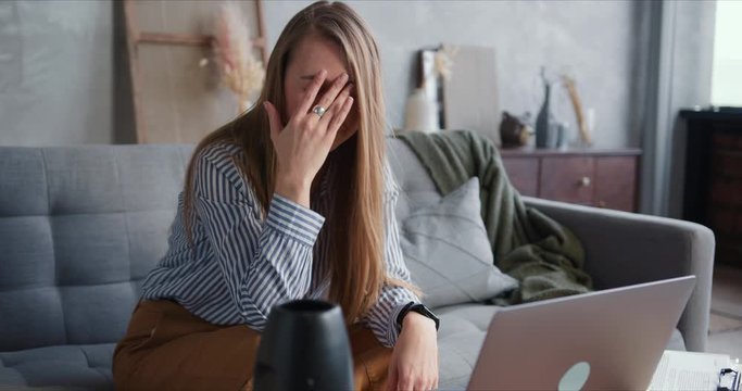 Young beautiful blonde business woman stressed and upset, struggling to use laptop for video work call from home.
