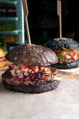 Brown hamburger with beef cutlet, tomatoes, cucumbers, red onions and wild berry sauce. Close-up. In the background is a black hamburger.
