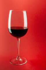 Glass with red wine. On a plain red background. Diffused light, soft shadows. Close-up. Place for text.