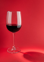 Glass with red wine. On a plain red background. Hard light, sharp shadows. Close-up. Place for text.
