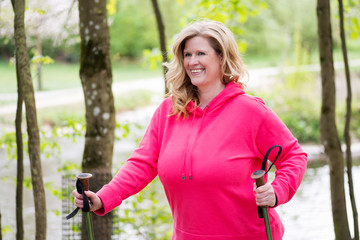 Attraktive Frau im mittleren Alter geht mit Walking-Stöcken in der Natur Spazieren 