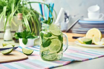 A glass of homemade lemon, lime, and mint lemonade sits on the wooden dining table. Cold, refreshing summer lemonade or mojito.