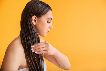 Beautiful young woman applying coconut oil on her hair against color background