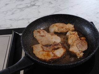 frying pan on an induction plate in which pork chops are baking