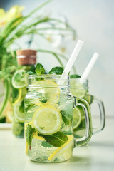 Two glasses and a bottle of homemade lemon, lime, and mint lemonade sit on the wooden dining table. Cold, refreshing summer lemonade or mojito.