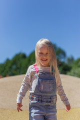 Fototapeta premium Blonde toddler girl playing on playground outdoors against blue sky
