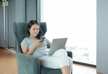 Young beautiful asian woman using smartphone and laptop computer working online at home and feel...
