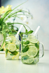 Two glasses of homemade lemon, lime, and mint lemonade sit on the wooden dining table. Cold, refreshing summer lemonade or mojito.
