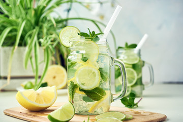 Two glasses of homemade lemon, lime, and mint lemonade sit on the wooden dining table. Cold, refreshing summer lemonade or mojito.