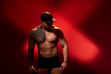 Young man posing on red background. Fitness man after workout. Inflated man with a tattoo in cap...