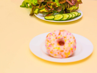 A donut or a salad. Salad on a plate. Chocolate donut. Health food. Dietary food. Choose between diet and junk food. Light background. The view from the top. Space for text.