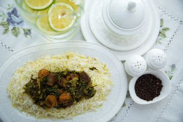 A bowl of white ceramic salt and pepper. Shah pilaf. Khan pilaf in a pita. Black pepper in a white ceramic pot . There is meat and plum chestnuts on the pilaf . Rice in a white plate. Sliced lemon .