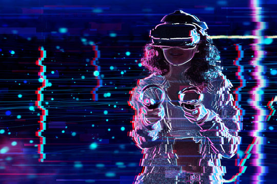 Teenage curly girl is playing in virtual reality game club. Smiling young woman in VR glasses is gaming, using wireless controllers. Entertainment and leisure concept. Modern technologies.