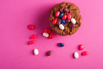 Homemade oat chocolate cookies stack with cereal with juicy jelly beans on minimal pink purple background, top view