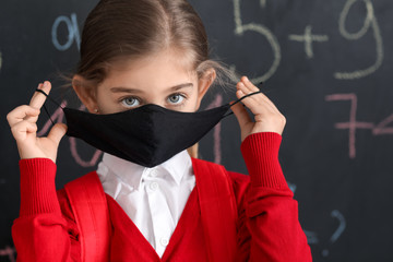 Little girl wearing medical mask near school blackboard