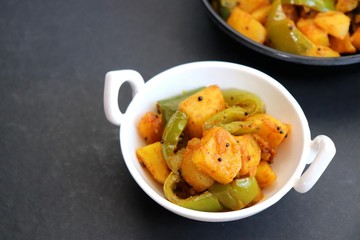 Indian food - Spicy Capsicum and potato stir fried with Indian spices. Aloo and Shimla Mirchi. served in black plate over moody background. 