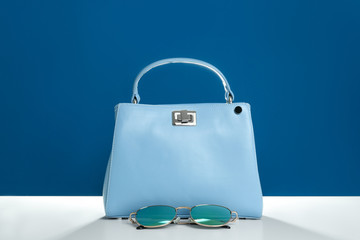 Stylish woman's bag and sunglasses on white table