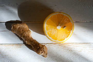 Lemon and ginger root lying on a wooden surface painted white and lit by the rays of the morning...