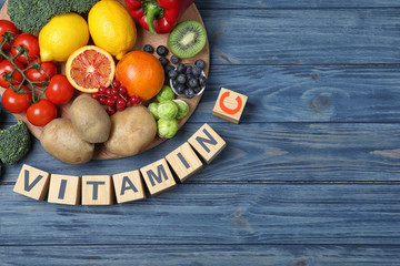 Cubes with phrase VITAMIN C and fresh products on blue wooden table, flat lay. Space for text