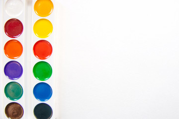 Top view on watercolor paint box framing border on white watercolor paper texture, creative art project, copy space