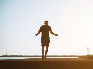 Young guy in shorts jumps on a rope on a sunny day on backgraund sky. Artistic effect. Blurred image