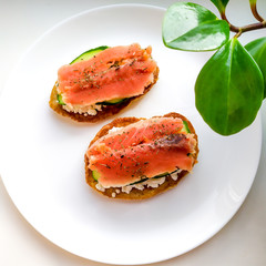 The concept of a healthy breakfast or snack.  Oat pancakes with cottage cheese, salmon and cucumber, sprinkled with dried basil on a white plate.