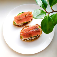 The concept of a healthy breakfast or snack.  Oat pancakes with cottage cheese, salmon and cucumber, sprinkled with dried basil on a white plate.