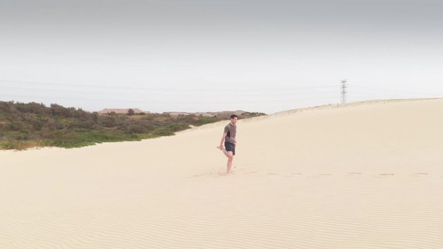 Aerial Flys Over Man Stretching Legs on Sand Dunes. Wide Shot