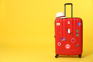 Red suitcase with travel stickers on yellow background. Space for text
