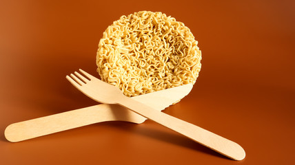 Raw instant noodles in the shape of a circle with a wooden disposable fork. pasta, for the preparation of which it is enough to pour boiling water and wait a few minutes. spaghetti. Copy space