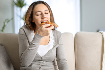 Beautiful young girl eating a slice of pizza at home