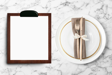 Table setting and empty menu on white marble background, flat lay. Space for text