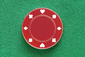 Red casino chip with playing card suits on the green textile table for poker. Gambling background texture