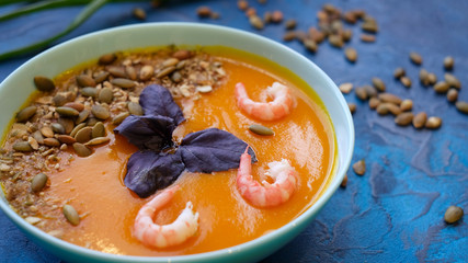 close up pumpkin soup with green onions and prawns on a blue background. Top View