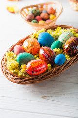 Multi-colored Easter eggs in a basket on a white wooden background