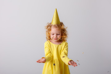 little girl blonde in a yellow dress catches confeti smiling happy on white background