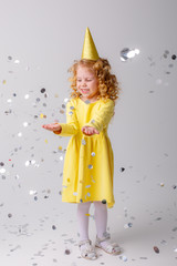 little girl blonde in a yellow dress catches confeti smiling happy on white background