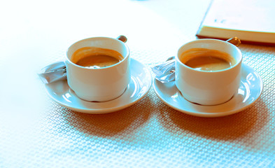 Two cups of white coffee on a saucer stand on a table in a cafe, sugar, next to a notebook. Breakfast for two. Morning. Love. Habits. Business people. Gourmet. Coffee lovers. Coffeeman. Close-up