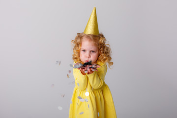 little girl blonde in a yellow dress catches confeti smiling happy on white background