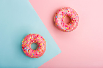 Pink tasty donuts decorated with colorful sprinkles on blue and pink background. Sweet donuts minimal flat lay. Flat lay. Top view
