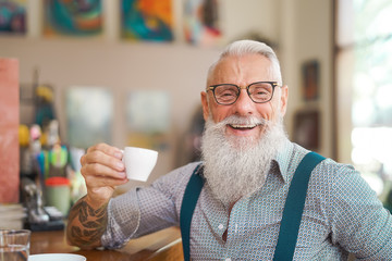 Happy smiling senior man drinking coffee in bar restaurant - Hipster trendy older male portrait -...