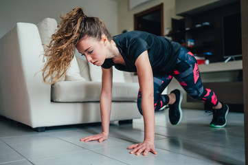 giovane bella ragazza fa sport a casa eseguendo esercizi a corpo libero. Smart gym e distanza sociale durante la pandemia 