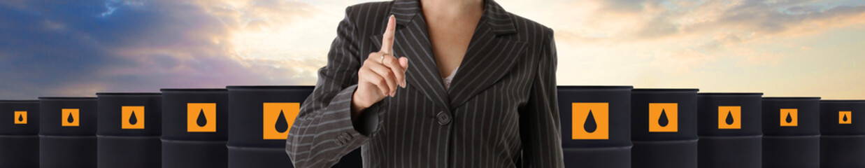 Businesswoman pointing on crude oil barrels against sky background. Crude oil and petroleum...